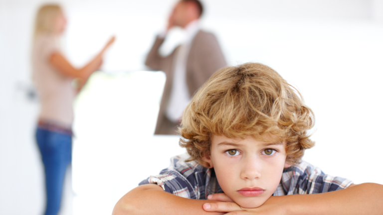 Niño triste con padres discutiendo de fondo, representando el impacto del divorcio en los niños